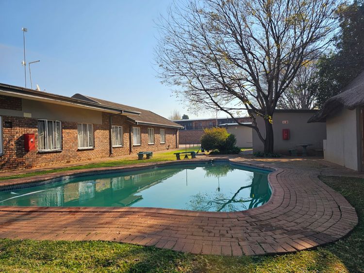 The swimming pool under a big tree, with the brick units behind it